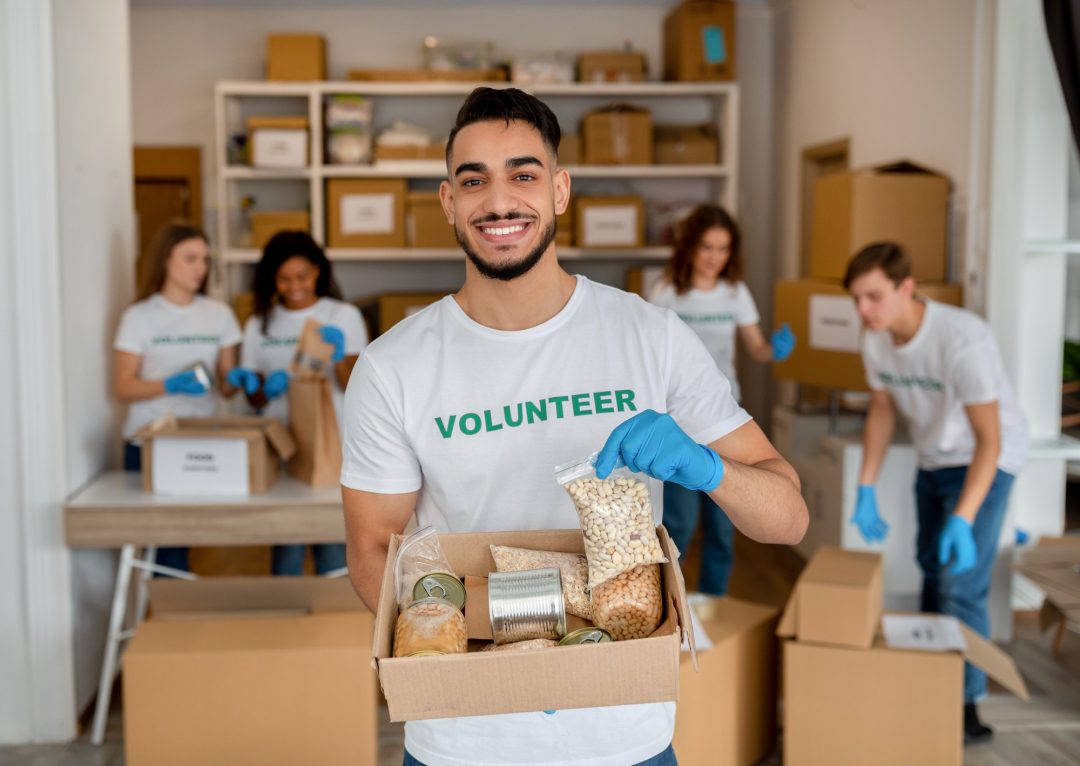 Young volunteer holding a food donation box and smiling at a charity center.