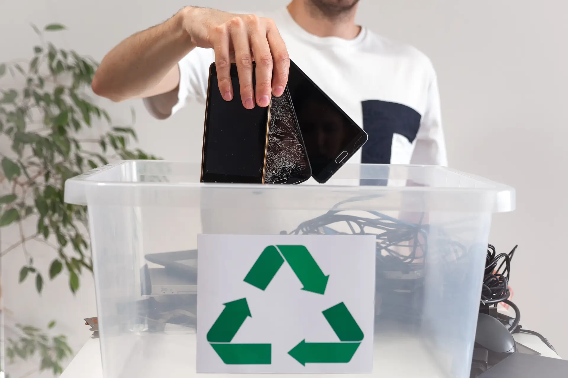 Person recycling broken smartphones into a bin with a recycling symbol, part of a veteran job training and e-waste sustainability program.